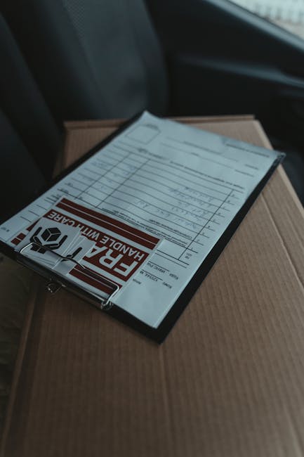 A close-up view of a house removal process inside a property, showing a cardboard box with a packing list or inventory sheet secured under a transparent plastic cover, resting on top of a larger cardb